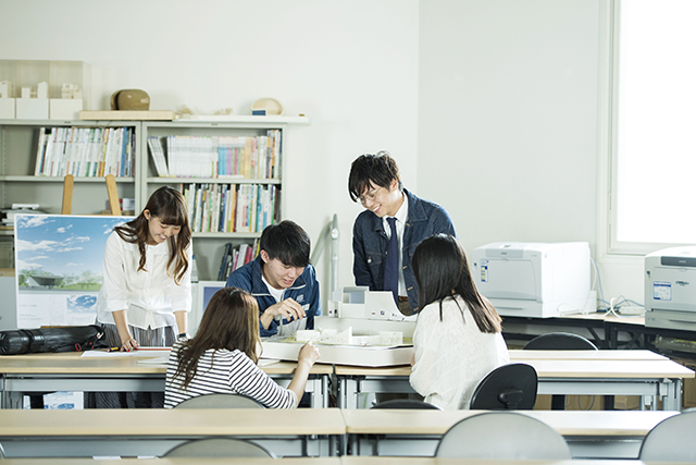 数人の学生が、建築模型を見ながら会話している写真